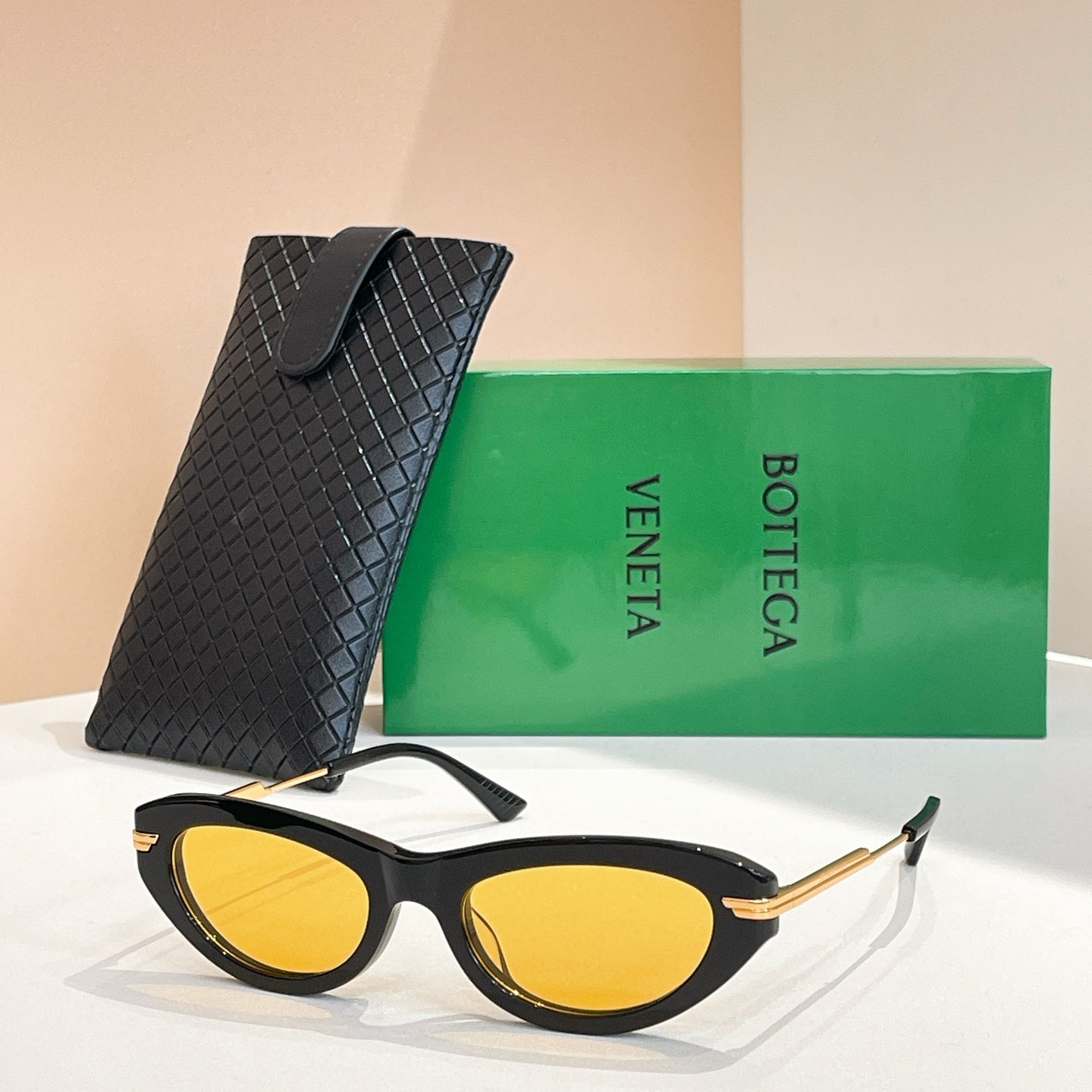 Black cat-eye sunglasses with gold-tone temples and yellow mirrored lenses, with black case