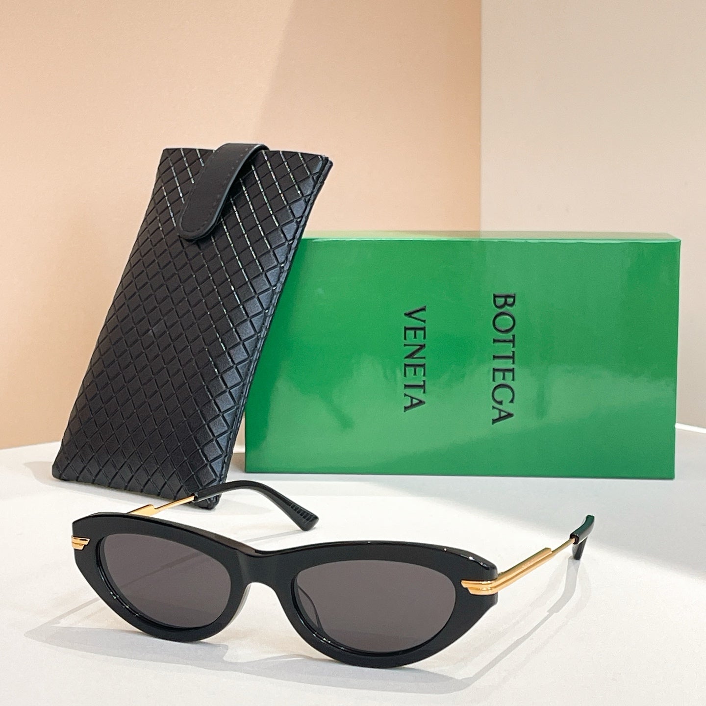 Black cat-eye sunglasses with gold-tone temples and dark lenses, with black textured case