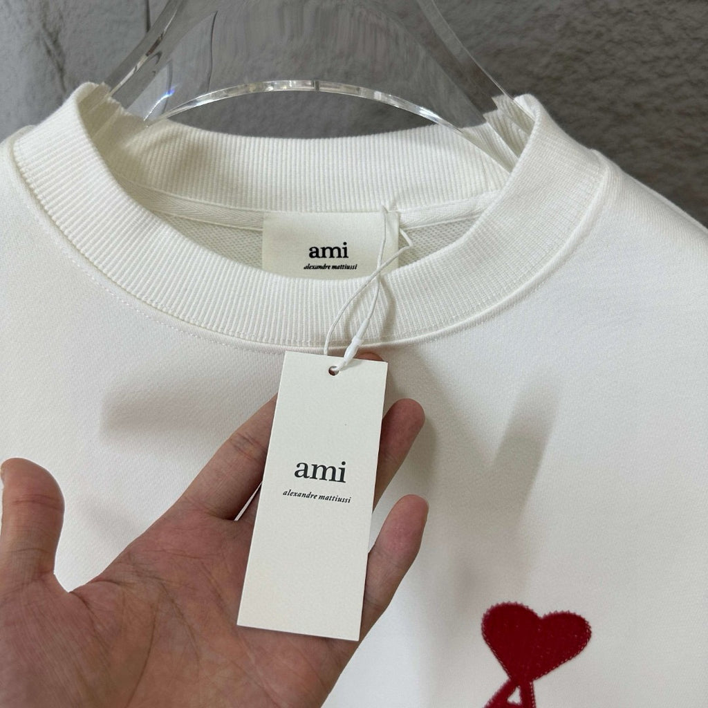 White crewneck sweatshirt with fabric tag at collar and red heart A logo