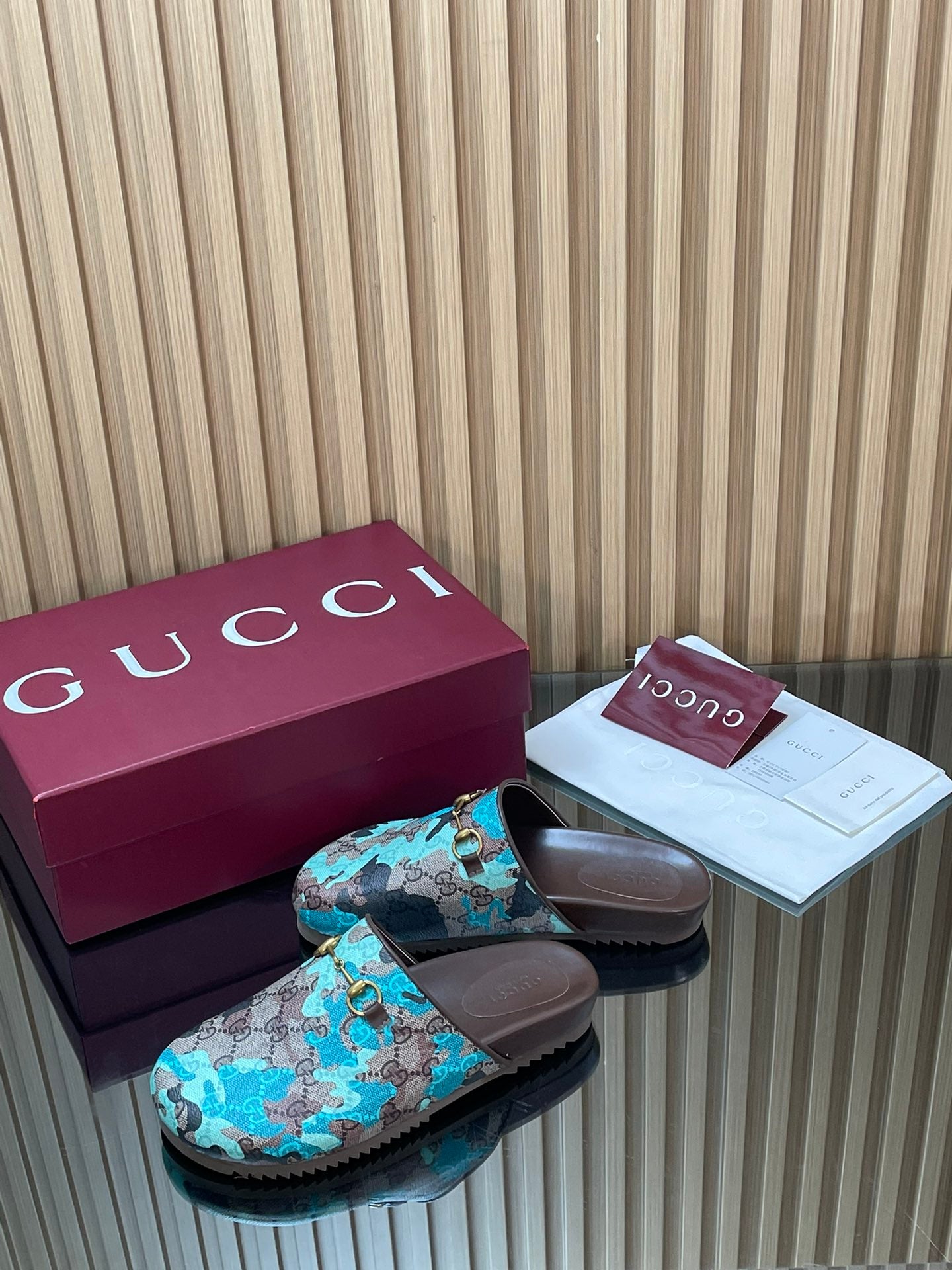 Gucci slide sandals with teal GG-pattern strap, gold buckle hardware, dark rubber soles.
