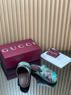 Gucci sandals on a ledge, teal GG-pattern upper with gold buckle and brown footbed.