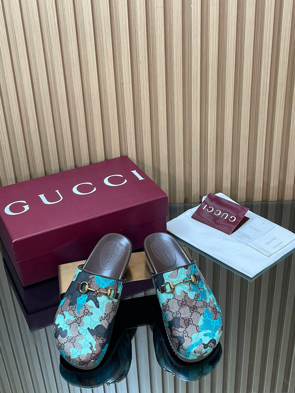 Gucci slide sandals with teal and brown GG-pattern upper, gold-tone buckle, dark sole.
