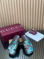 Gucci slide sandals with teal and brown GG-pattern upper, gold-tone buckle, dark sole.