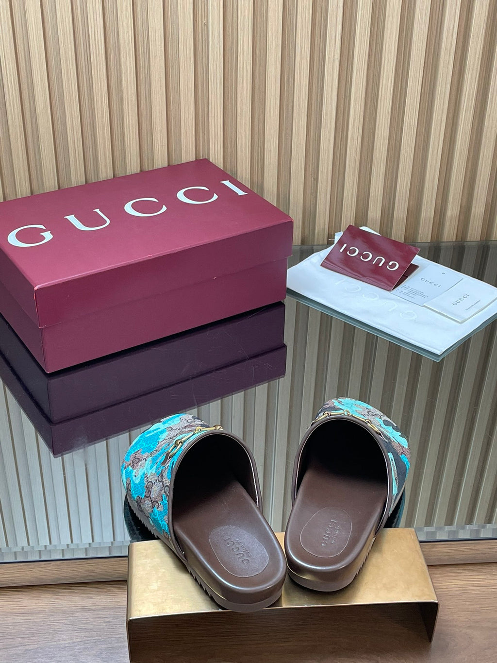 Gucci slide sandals showing open toe, teal GG-pattern upper with gold buckle on brown base.