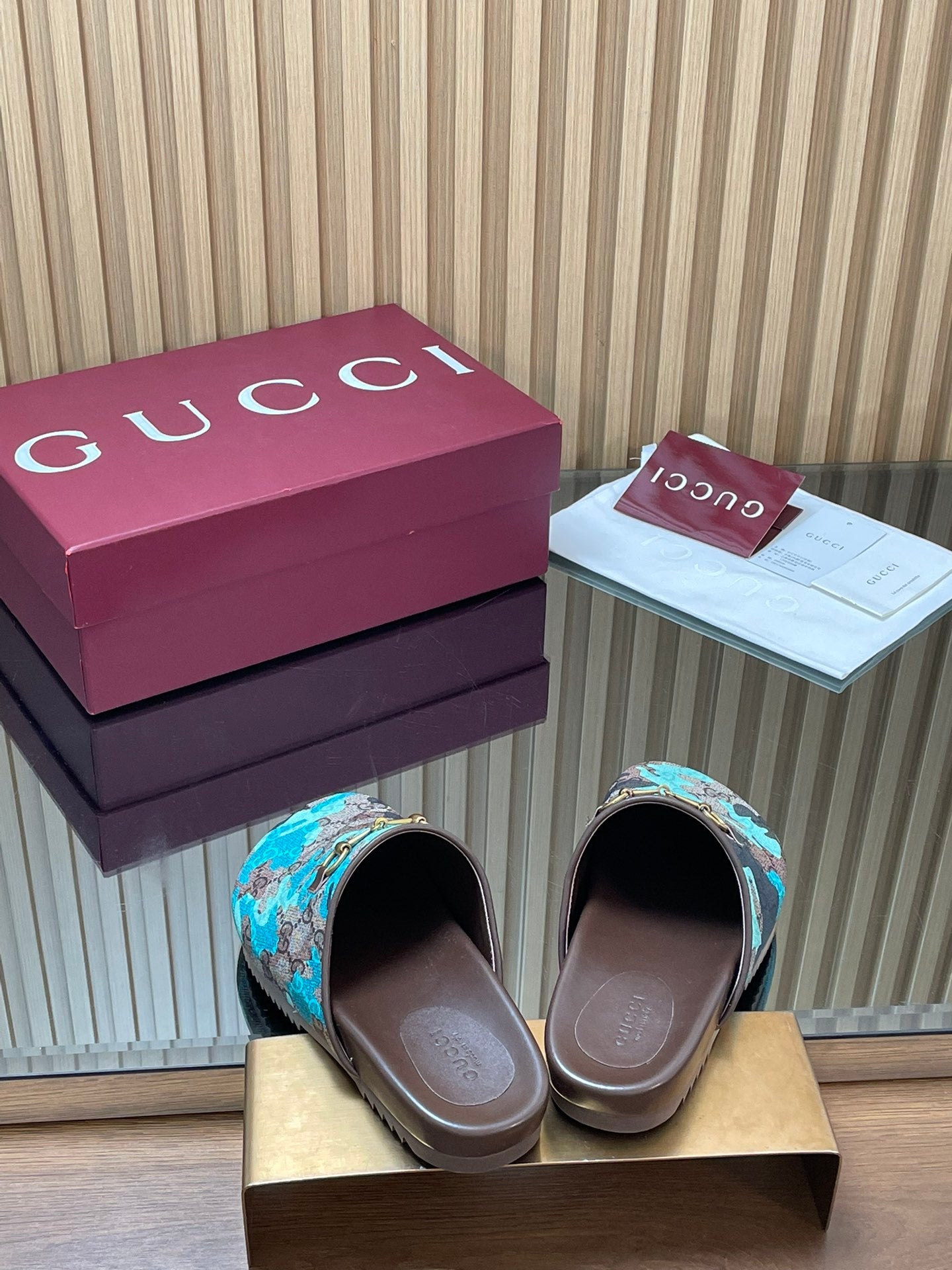 Gucci slide sandals showing open toe, teal GG-pattern upper with gold buckle on brown base.