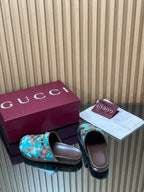 Gucci slide sandals with teal GG-pattern straps, gold buckle, showing inner brown footbeds.