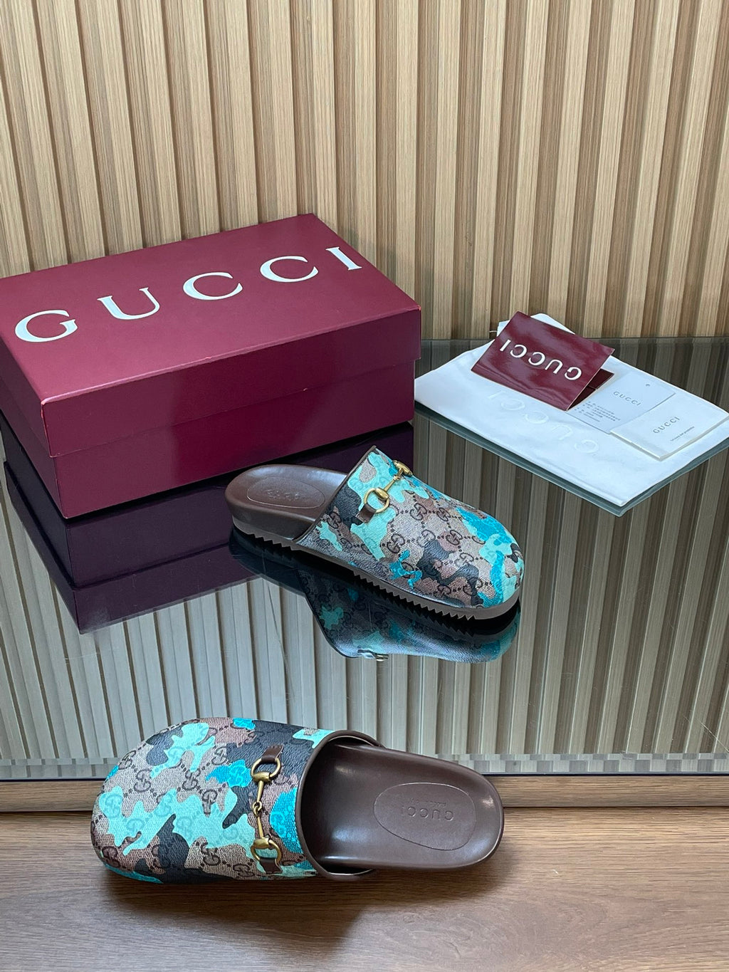 Gucci slide sandal pair, teal and brown GG-pattern straps with gold-tone buckle detail.