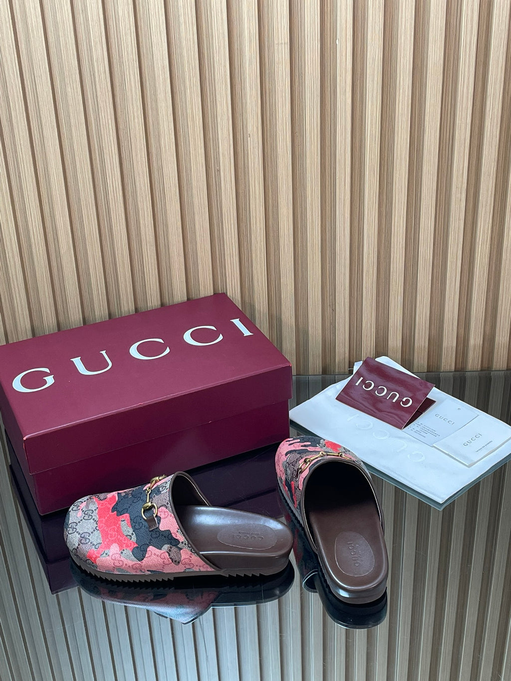 Gucci slide sandals with patterned upper and metal logo buckle, side-by-side pair