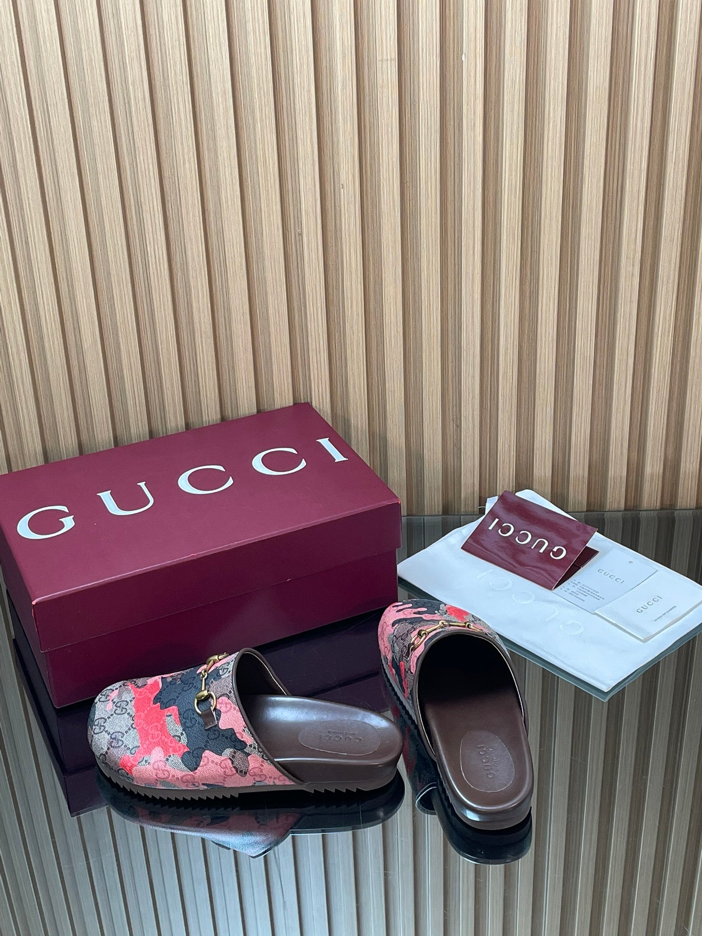 Gucci slide sandals with patterned upper and metal logo buckle, side-by-side pair