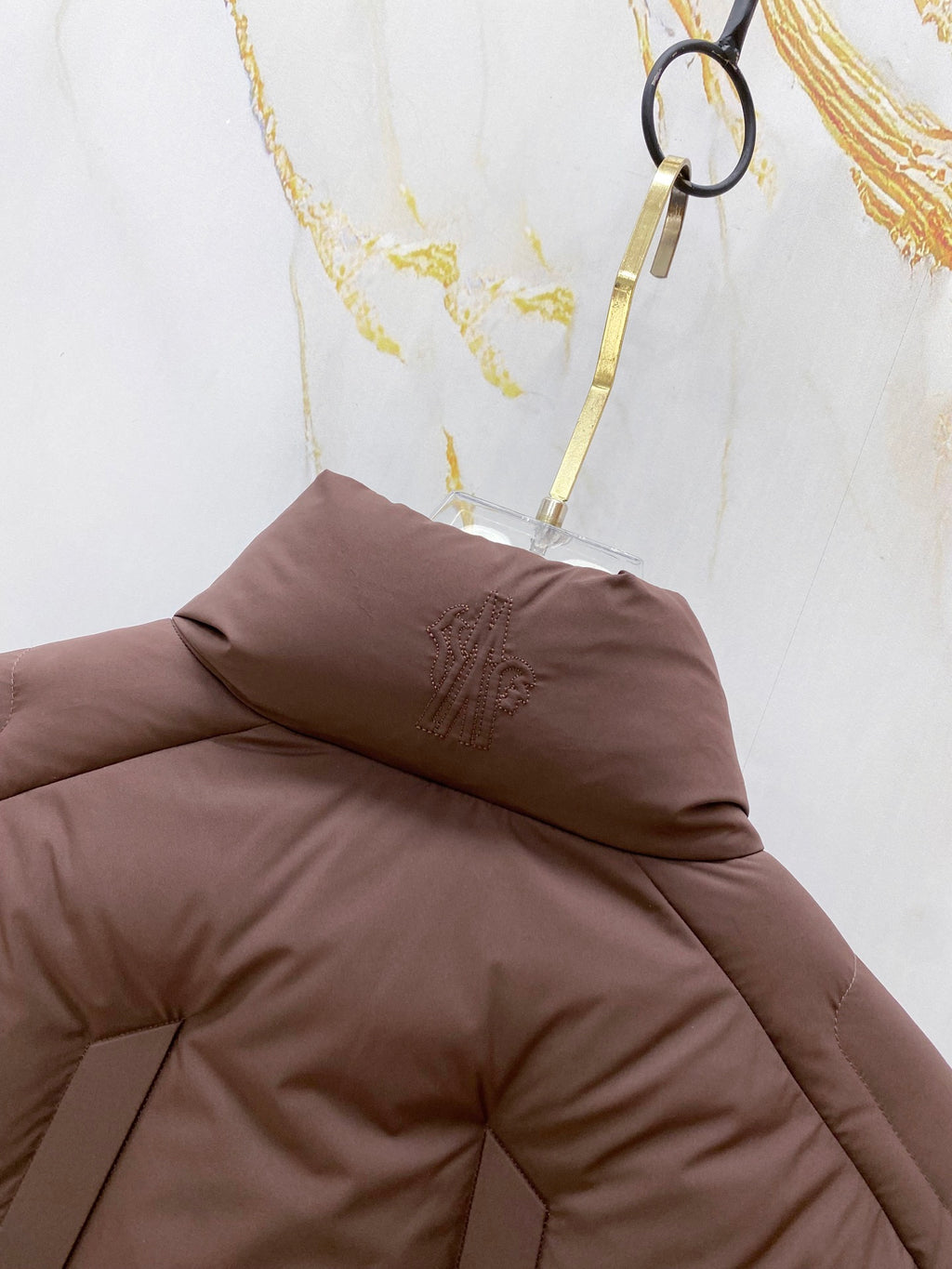 Moncler puffer jacket hood and collar detail, dark brown padded fabric.