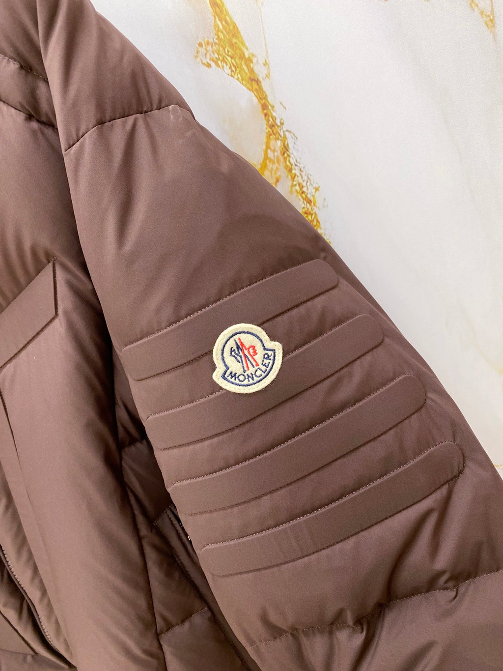 Moncler puffer jacket sleeve patch, dark brown with round logo emblem.