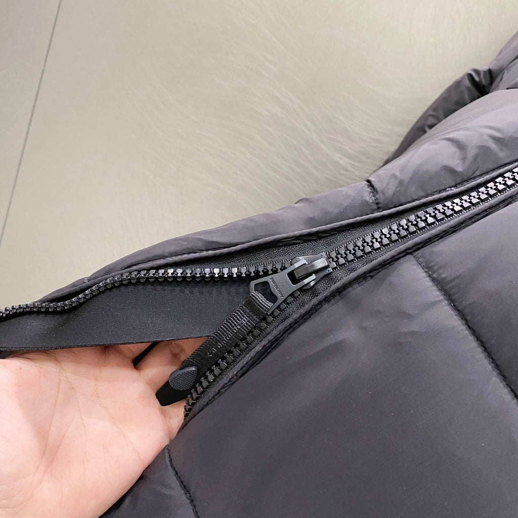 Puffer jacket zipper close-up with dark gray tape and metal pull, quilted fabric panel.