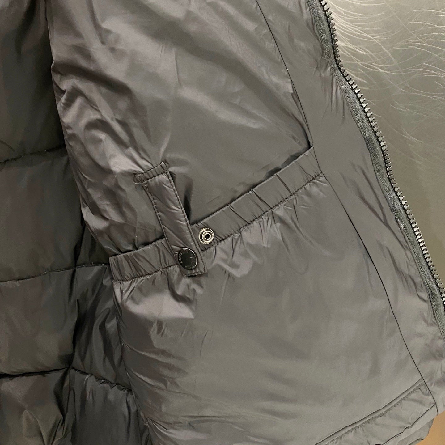 Puffer jacket inner lining close-up with snap button and stitched pocket seam.
