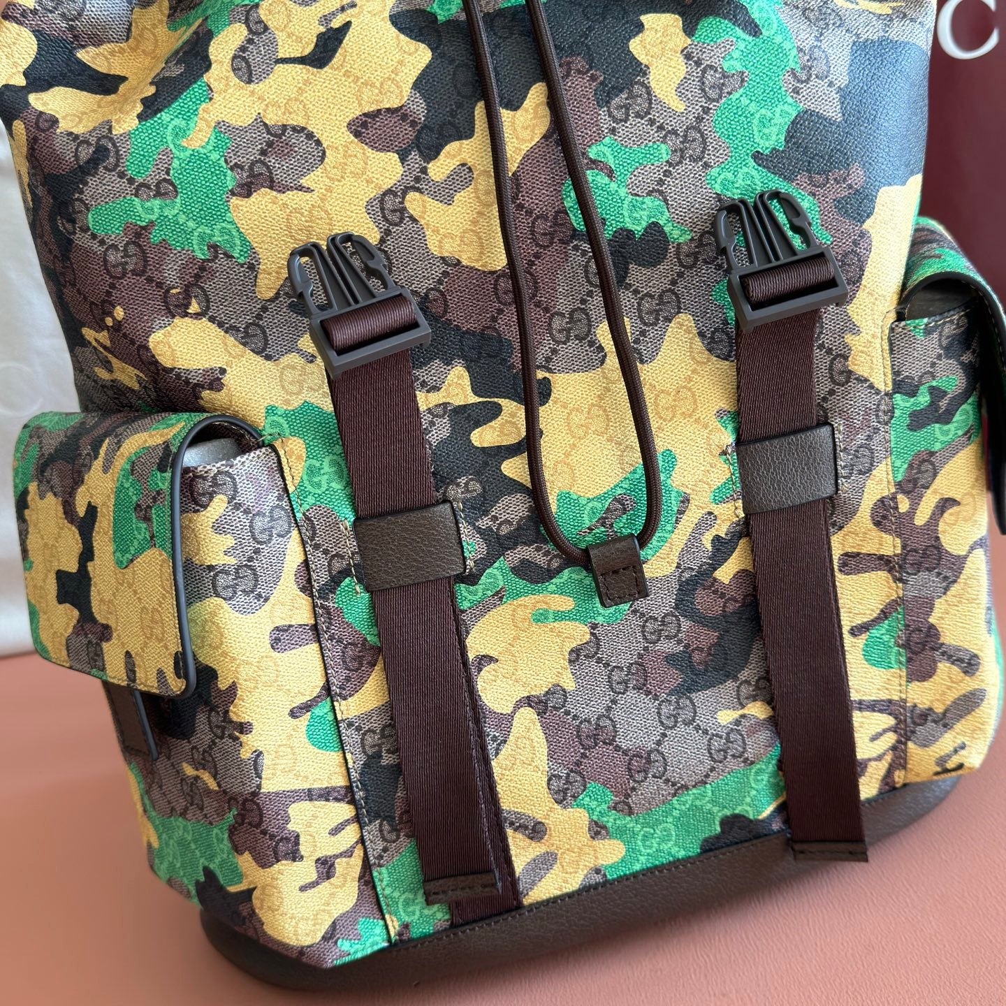Camo backpack front with brown strap buckles and hanging cords
