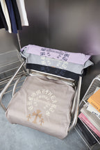 Stack of folded T-shirts in light gray and lavender with embroidered back graphic.