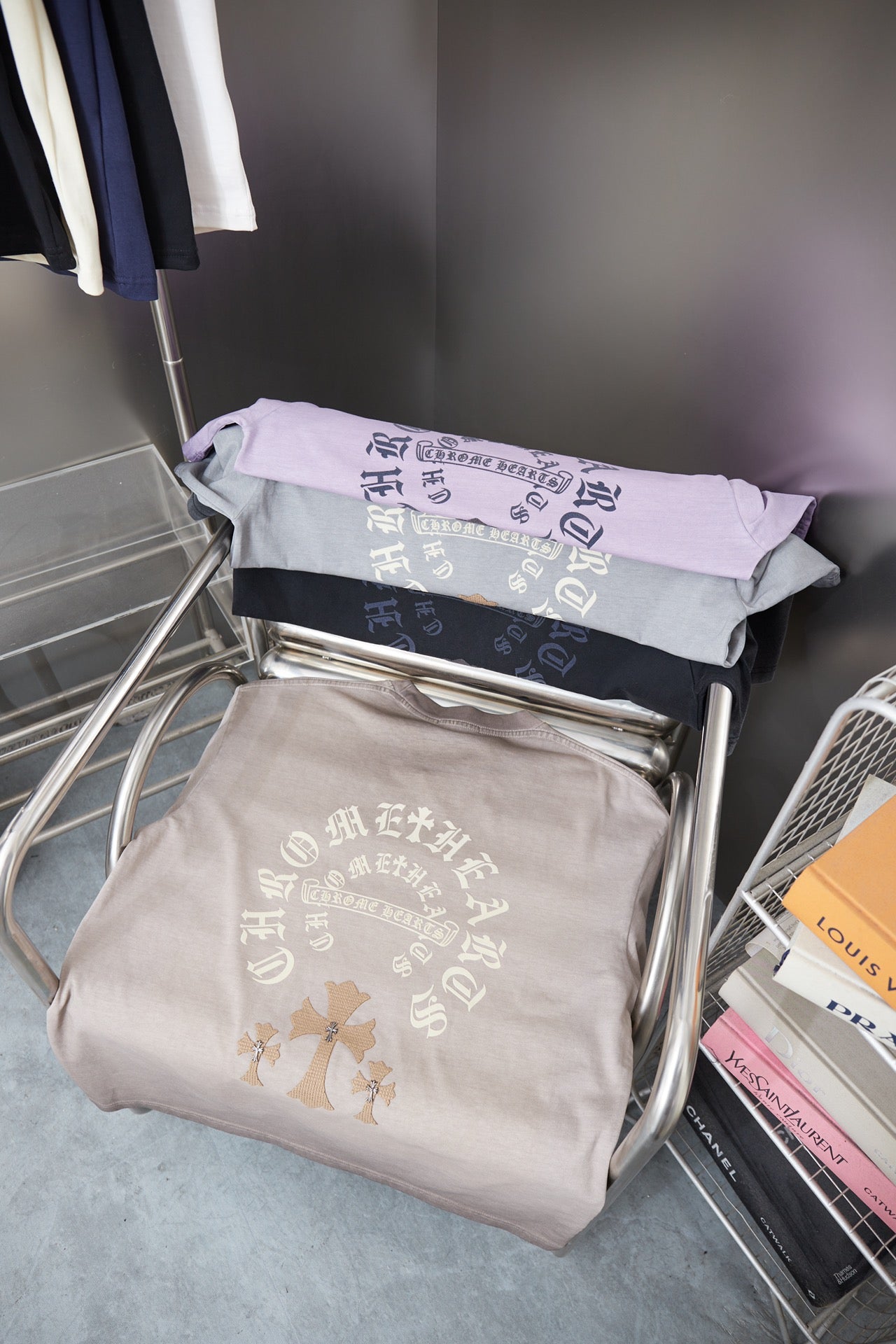 Stack of folded T-shirts in light gray and lavender with embroidered back graphic.