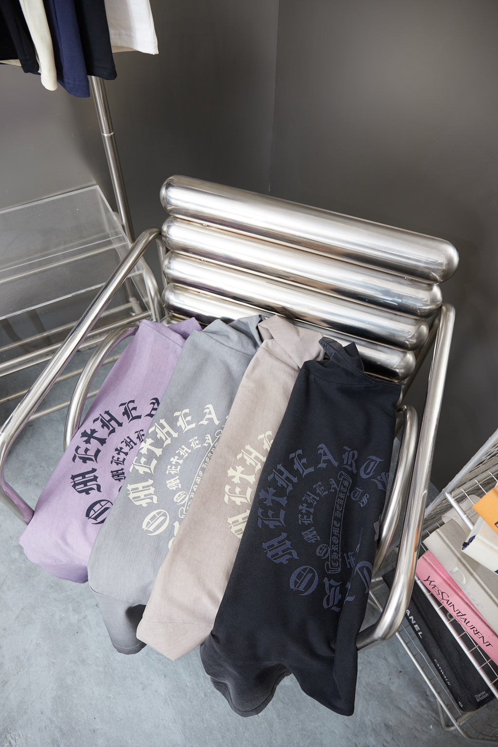 Folded T-shirts in light purple, gray, and black hanging on chrome rack