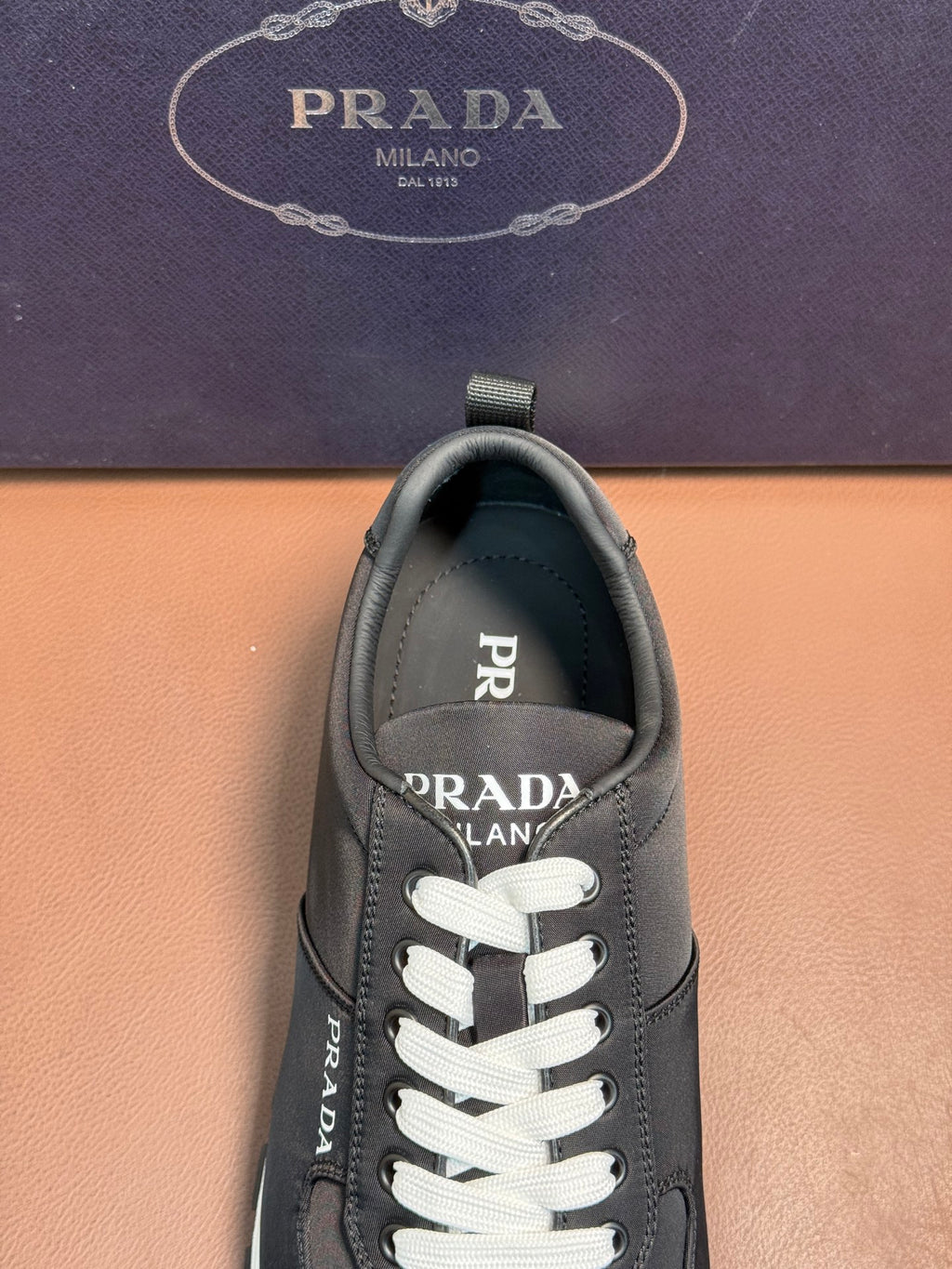 Black Prada sneaker upper close-up, lace-up front with white laces and brand patch