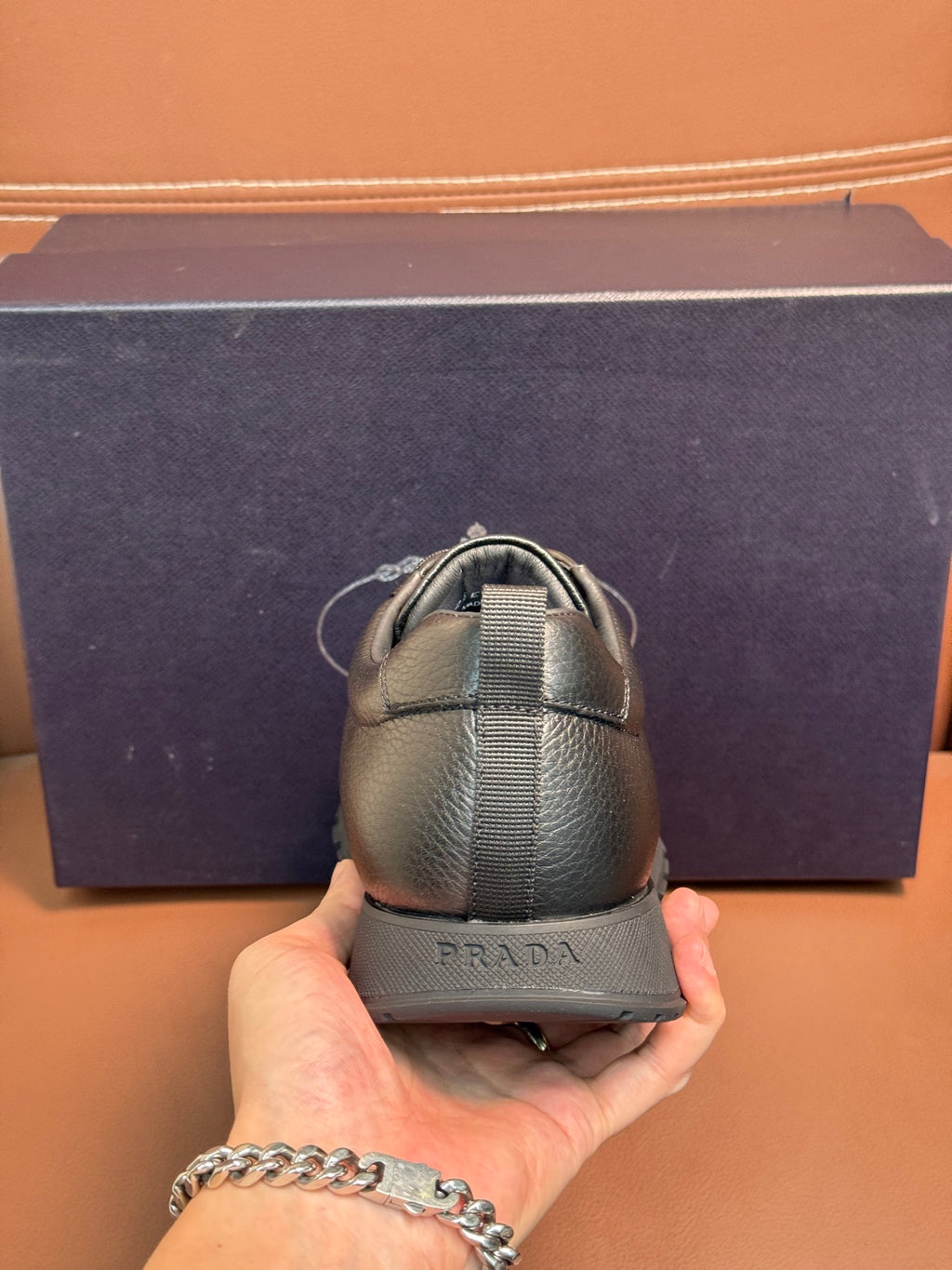 Dark leather lace-up sneaker held by hand, showing heel with elastic strap