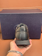 Dark leather lace-up sneaker held by hand, showing heel with elastic strap