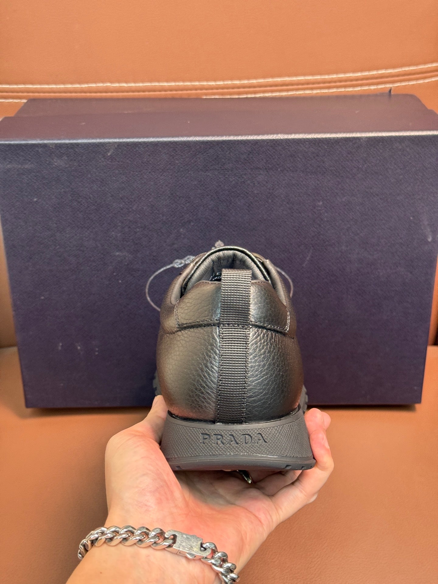 Dark leather lace-up sneaker held by hand, showing heel with elastic strap