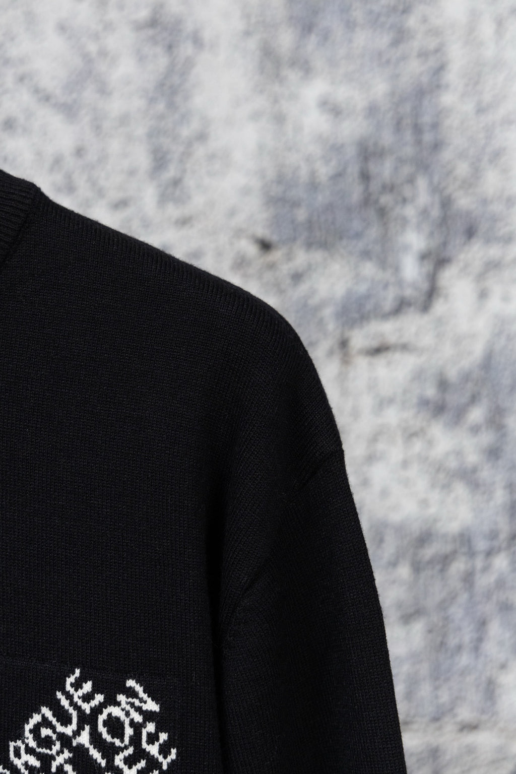 Black sweater sleeve with partial white embroidered logo on knit fabric