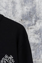 Black sweater sleeve with partial white embroidered logo on knit fabric