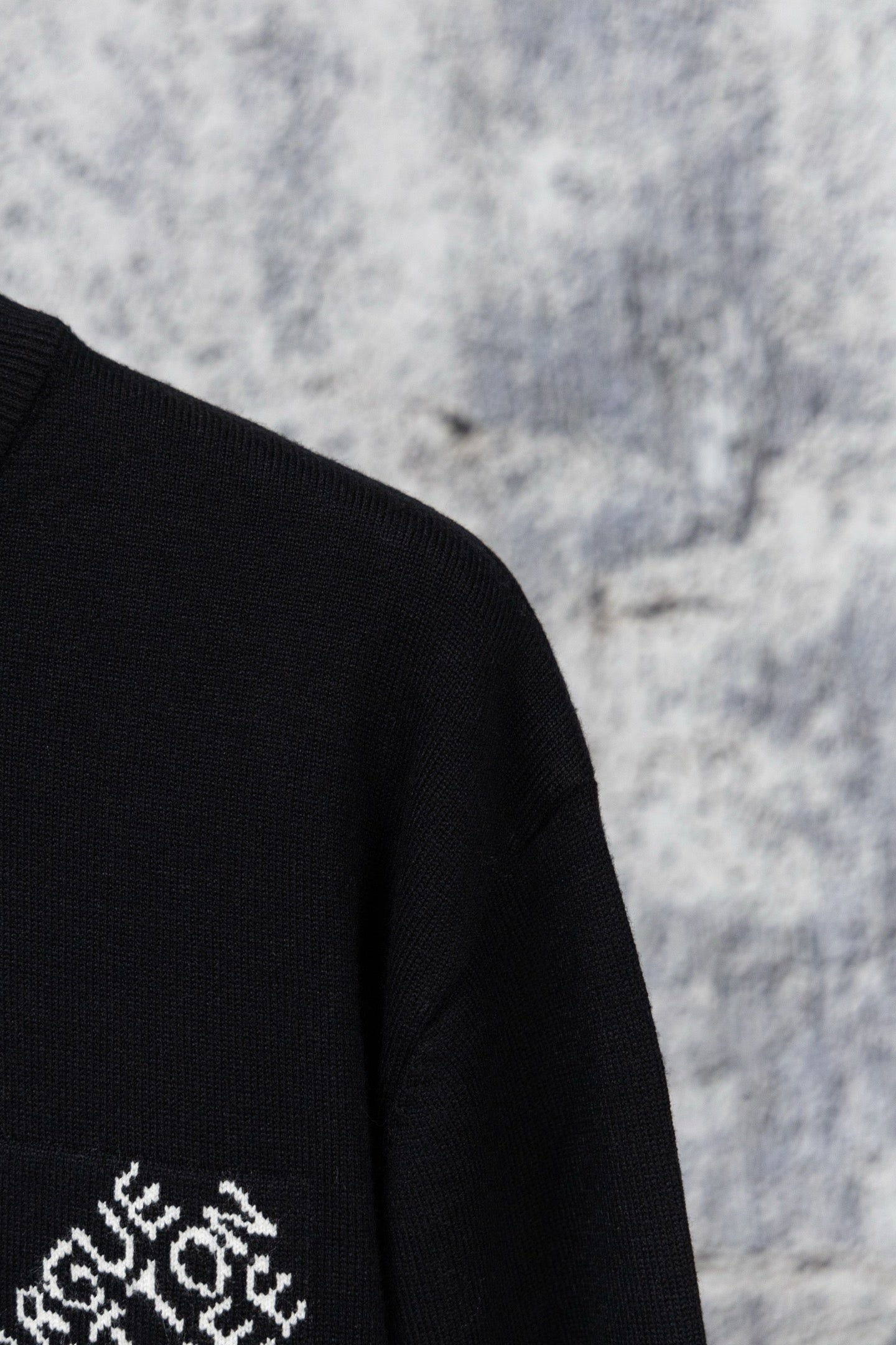 Black sweater sleeve with partial white embroidered logo on knit fabric