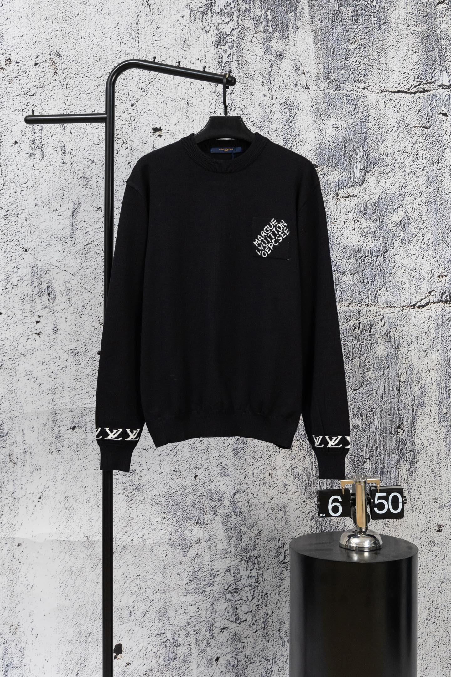 Black knit sweater with crew neck and small white logo detail at chest