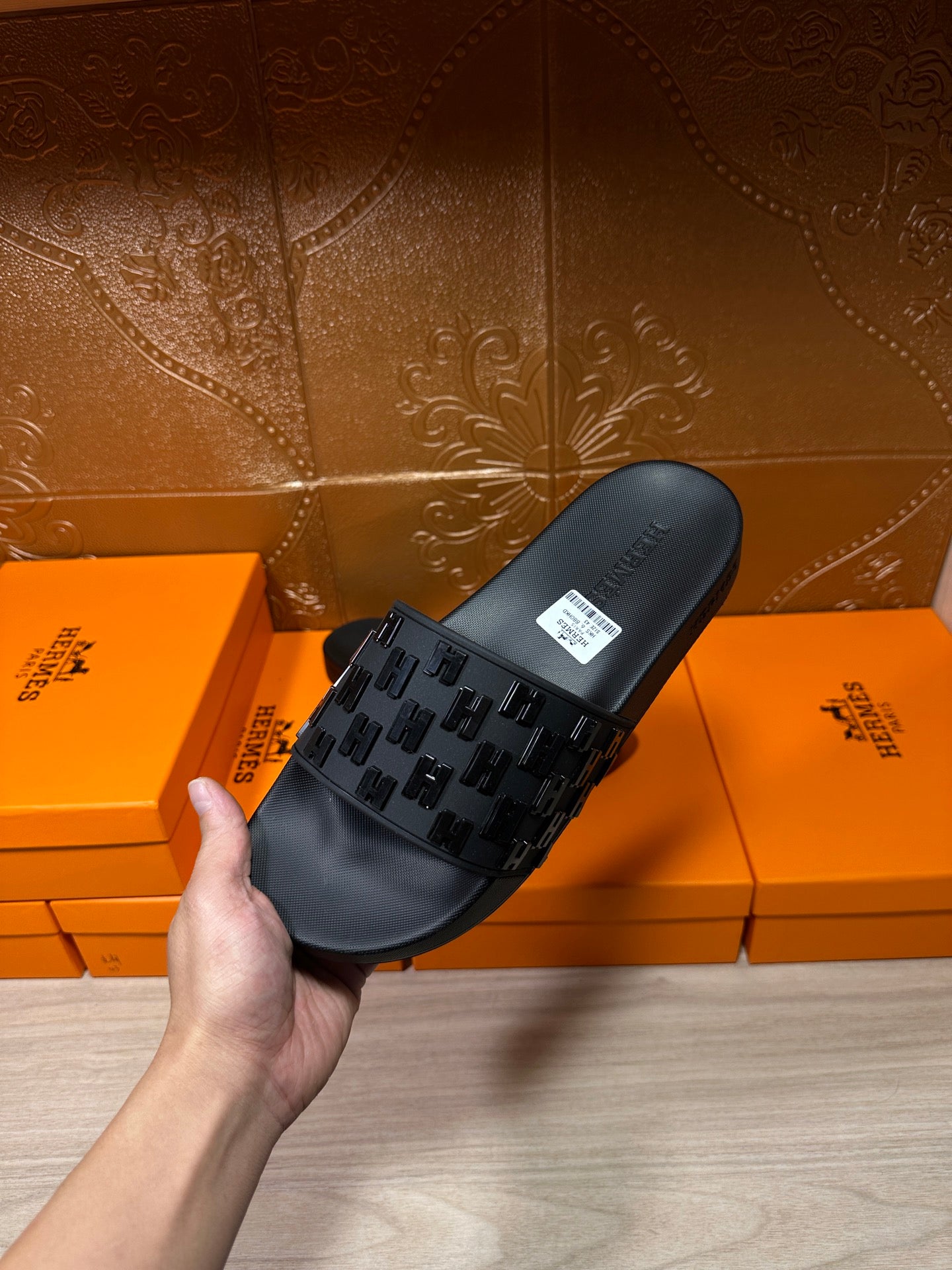 Hermes black slide sandal held in hand, textured top strap and white tag