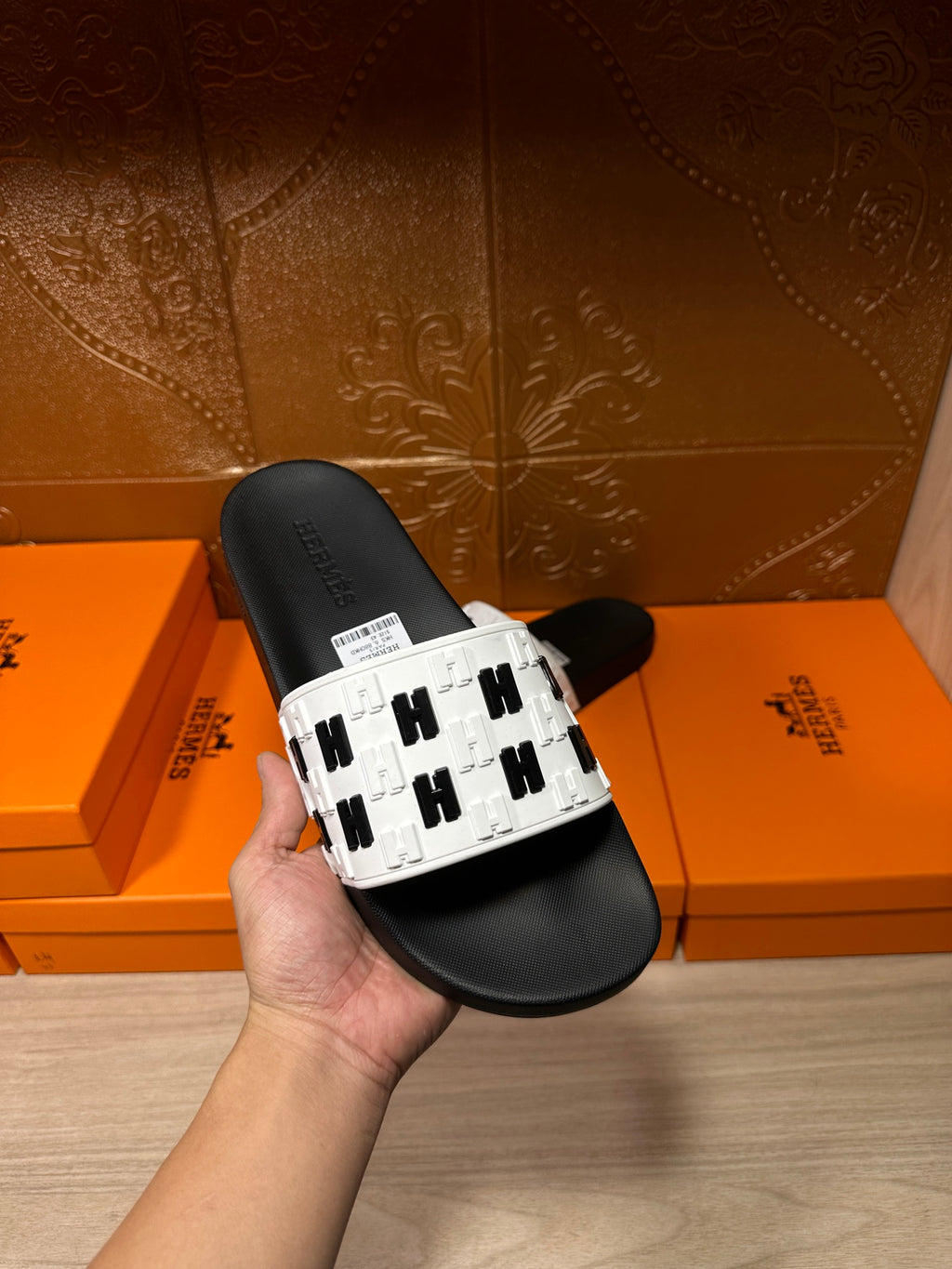Hand holding a black slide sandal with a white logo-print strap and black sole