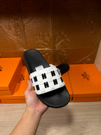 Hand holding a black slide sandal with a white logo-print strap and black sole