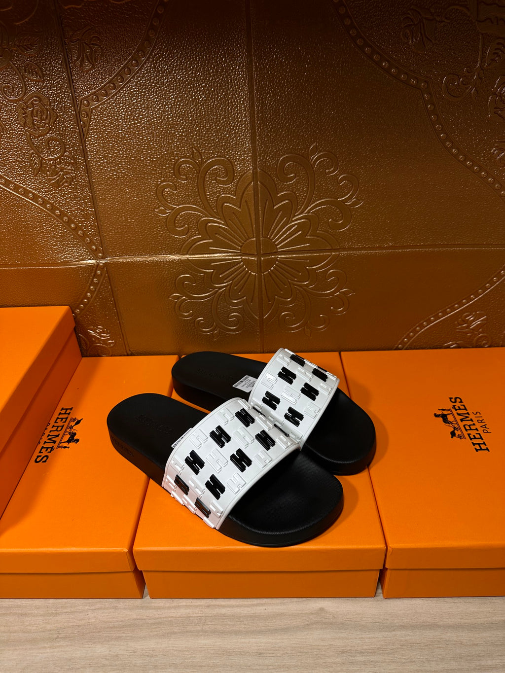 Black and white slide sandals laid on orange boxes with logo-print straps