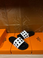 Side view of black slide sandals with white patterned straps and black soles