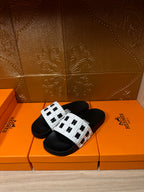 Black slide sandals with white patterned straps and adjustable buckle detail