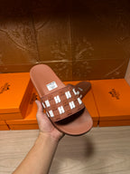 Hermes dark brown slide sandal held in hand, showing patterned H strap and label
