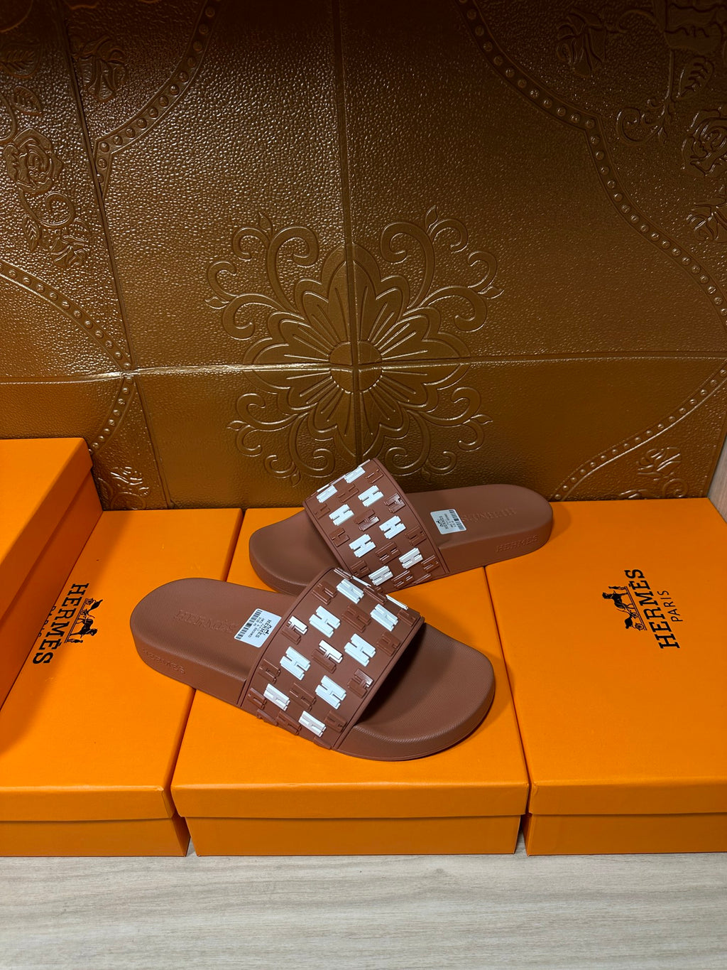 Hermes dark brown slide sandals with patterned strap over a smooth, flat footbed