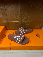 Hermes dark brown slide sandals with patterned strap over a smooth, flat footbed