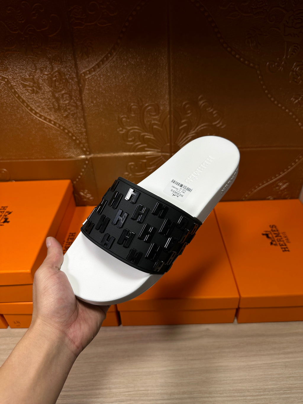 Hermes slide sandal held in hand, white footbed with black patterned strap close