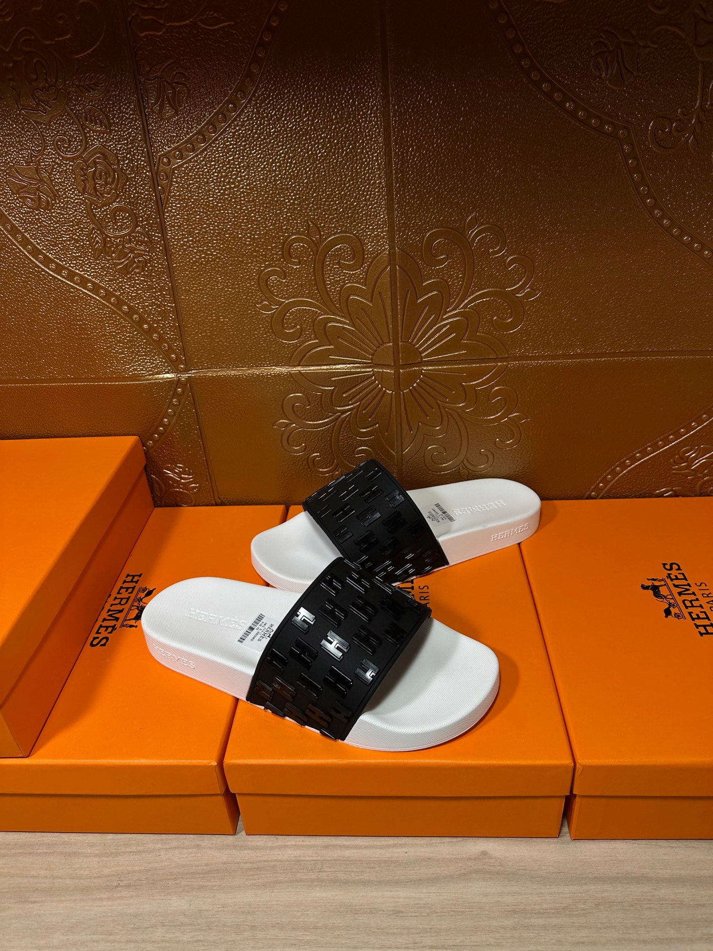 Hermes slide sandals on an orange box, black patterned strap over white footbed
