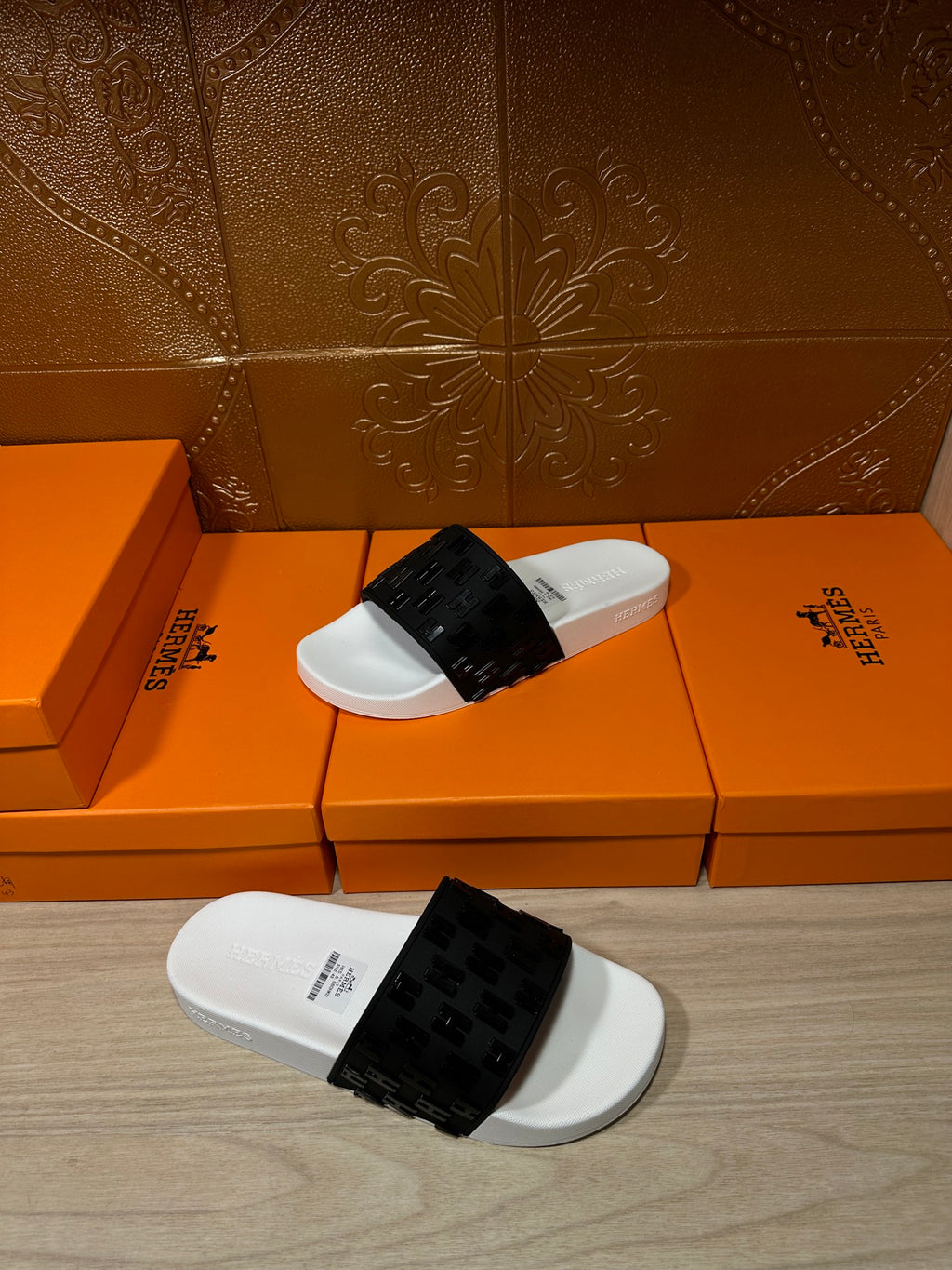 Hermes slide sandals laid on the floor, white footbed with black patterned strap