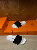 Hermes slide sandals laid on the floor, white footbed with black patterned strap