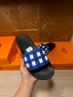 Hermes slide sandals held in hand: black sole with blue patterned strap
