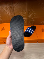 Hermes slide sandal outsole view: textured black sole with H pattern; blue strap visible