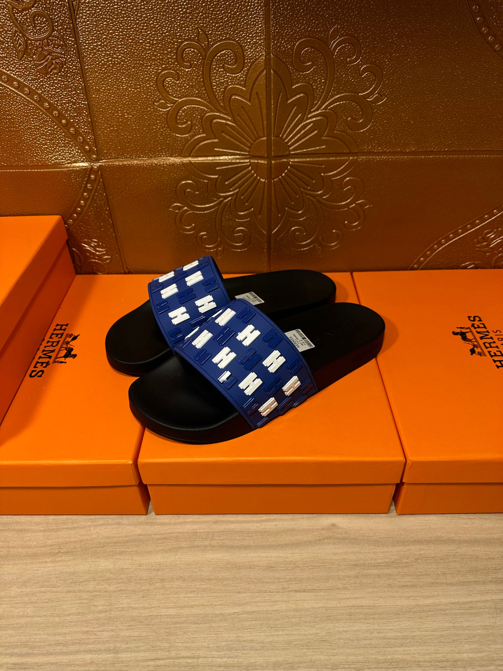 Hermes slide sandals, blue patterned strap with white H motifs and black sole, angled view