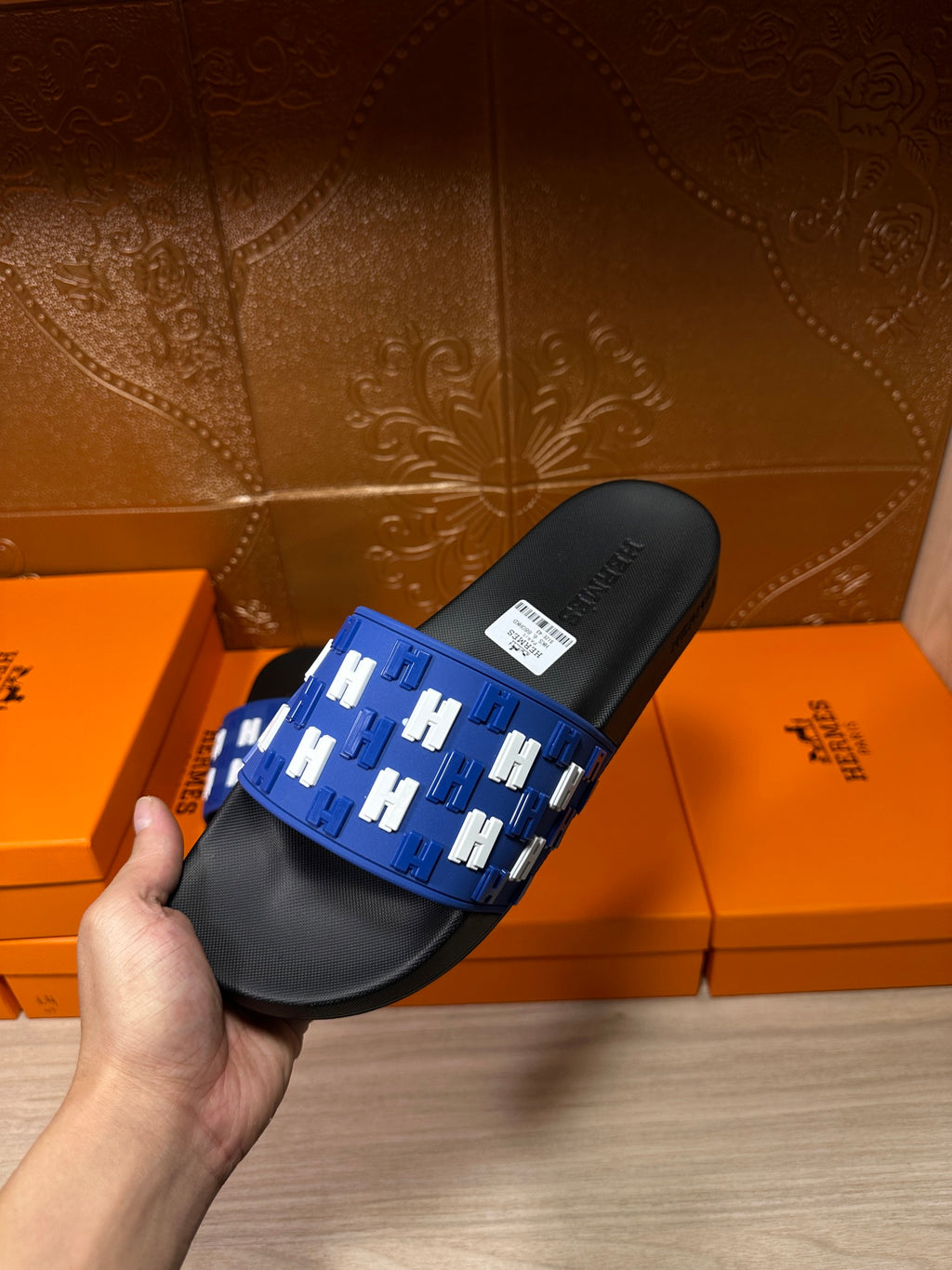 Hermes slide sandals held, showing blue strap with white H pattern and black footbed