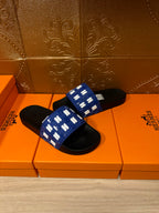 Hermes slide sandals with blue patterned strap and black sole, side-by-side on box