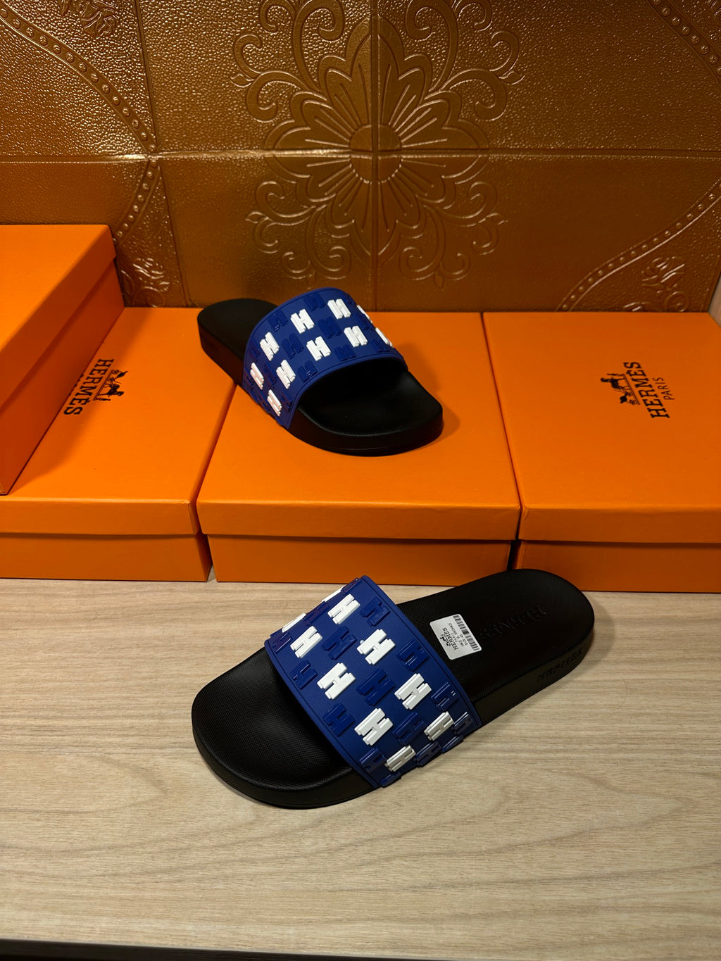 Hermes slide sandals, blue strap with white H pattern and black footbed, stacked angle
