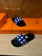 Hermes slide sandals, blue strap with white H pattern and black footbed, stacked angle