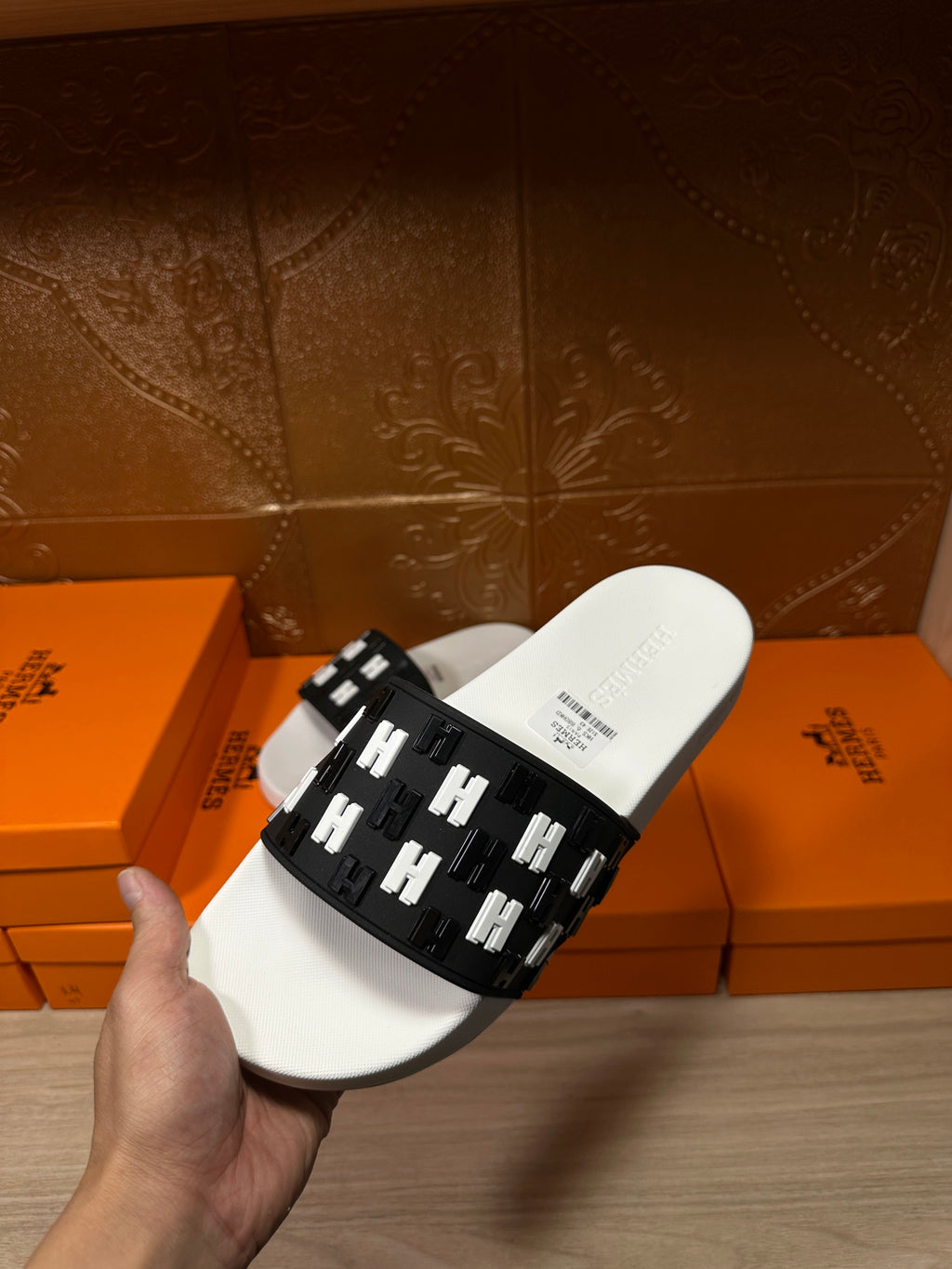 Hermes slide sandals held up; white sole with black strap featuring repeating H icons